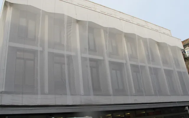 White protective debris netting wrapping a multi-storey building facade